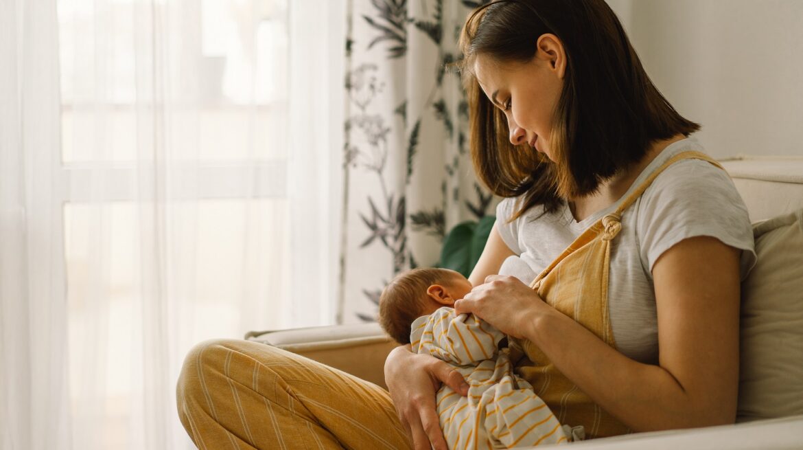 Newborn baby boy sucking milk from mothers breast. Portrait of mom and breastfeeding baby.