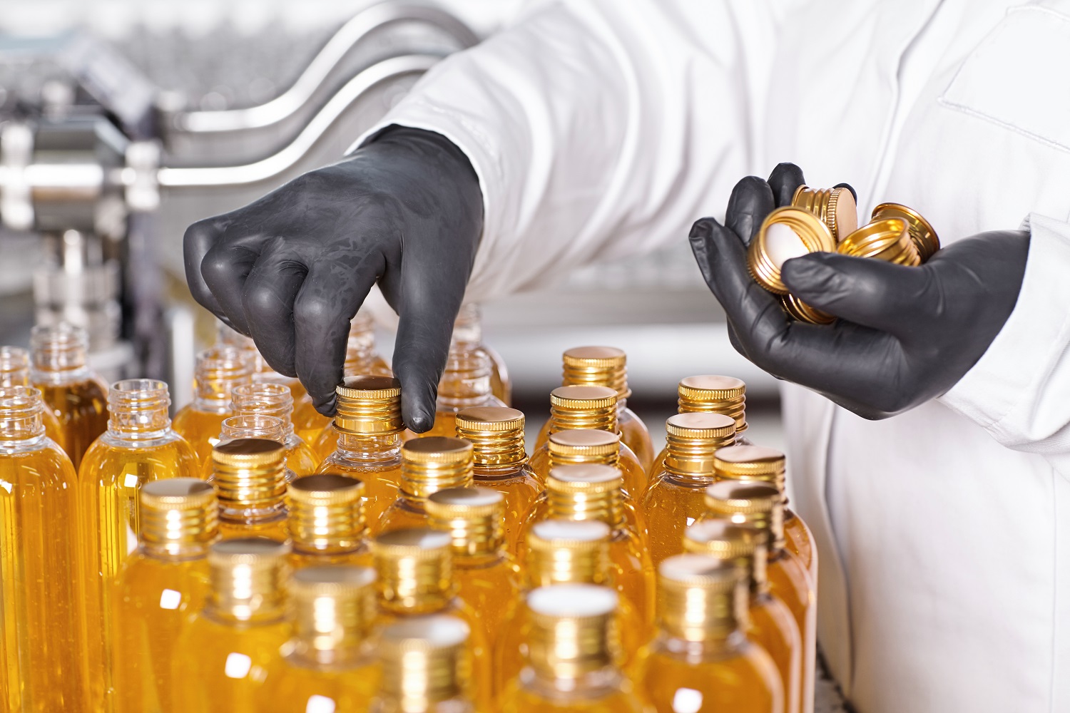Laboratory worker wearing white medical gown and black rubber gloves holding robs in one hand and twisting glass bottles with yellow thick liquid. Medical professional worker creating new products
